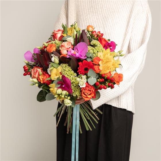 Person holding a vibrant bouquet of flowers against a neutral background