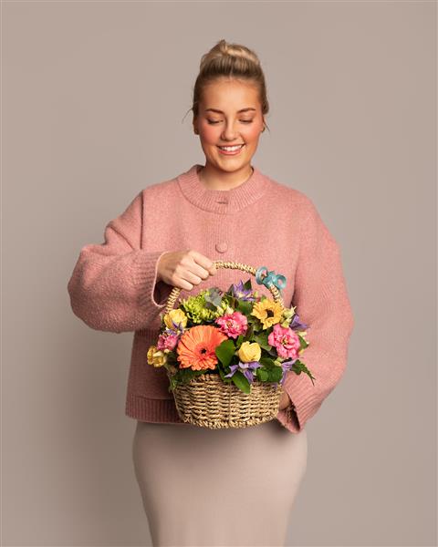 Woman holding a basket of bright flowers against a plain background