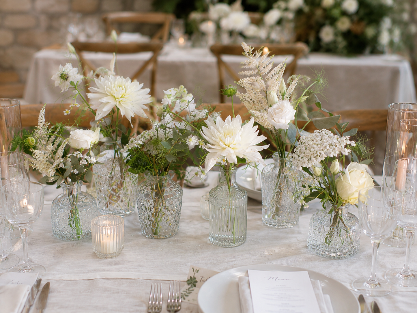 Elegant wedding table styled with ivory floral bud vases, glass bottles, foliage and candlelight centrepieces for a romantic boho wedding reception.
