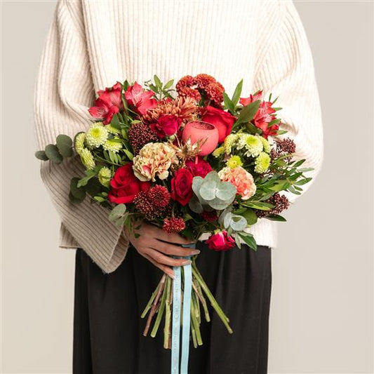Person holding a  bouquet of red and green flowers   with roses against a neutral background