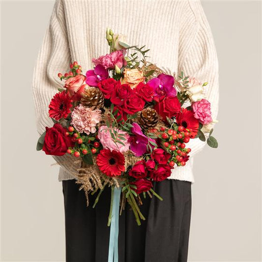 Person holding a red sumptuous bouquet of orchids roses and other flowers against a neutral background