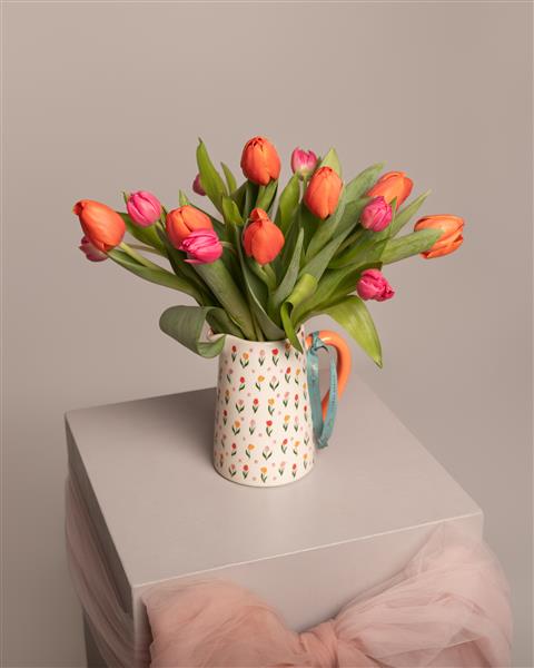 Vase with pink and orange tulips on a light surface with a neutral background