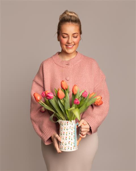 Woman holding a vase of colorful tulips against a plain background