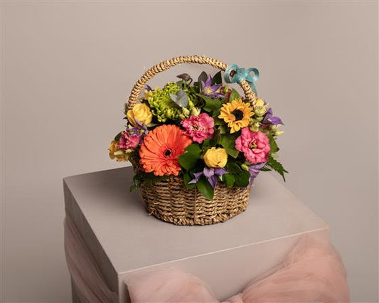 Colorful flower arrangement in a woven basket on a light surface with a neutral background