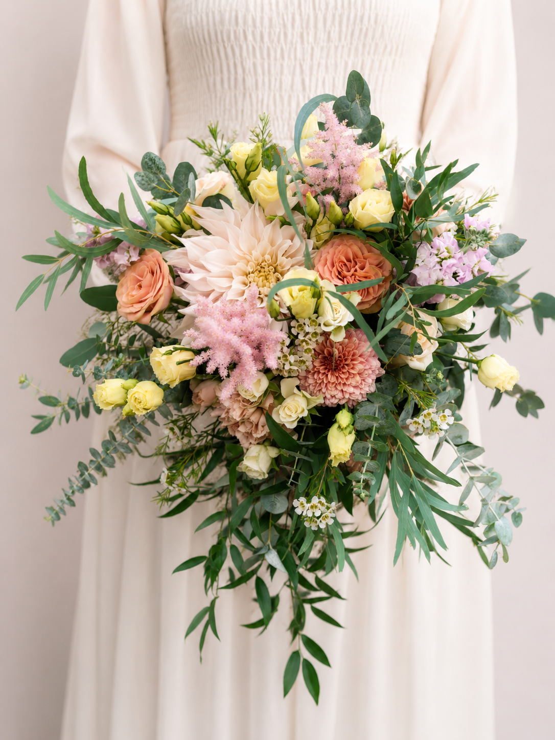 a cascading bridal bouquet of eucalyptus astilbe dahlia roses and wax flower held by a bride in white dress
