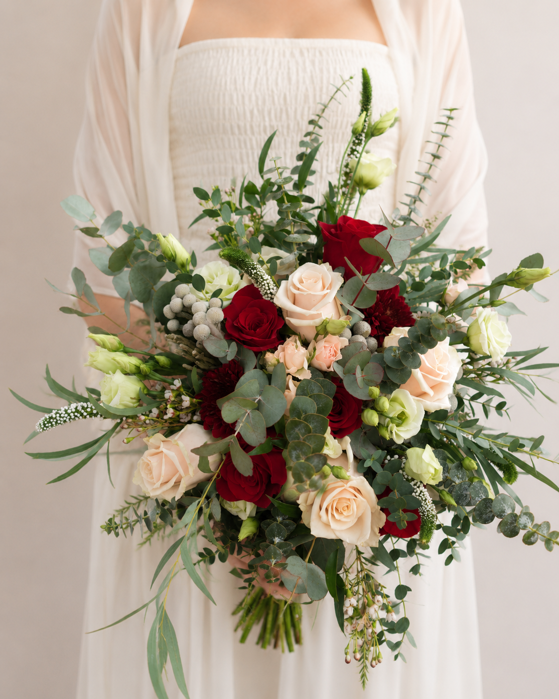 Bride holding Burgundy Blush Bridal Bouquet featuring burgundy roses, blush roses, spray roses, brunia berries and eucalyptus foliage.