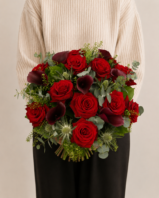 Bouquet of red and burgundy roses with greenery held by a person wearing a beige sweater.