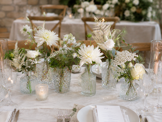 Elegant wedding table styled with ivory floral bud vases, glass bottles, foliage and candlelight centrepieces for a romantic boho wedding reception.