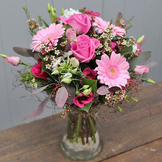 Bouquet of pink flowers in a clear vase on a wooden surface with a gray background