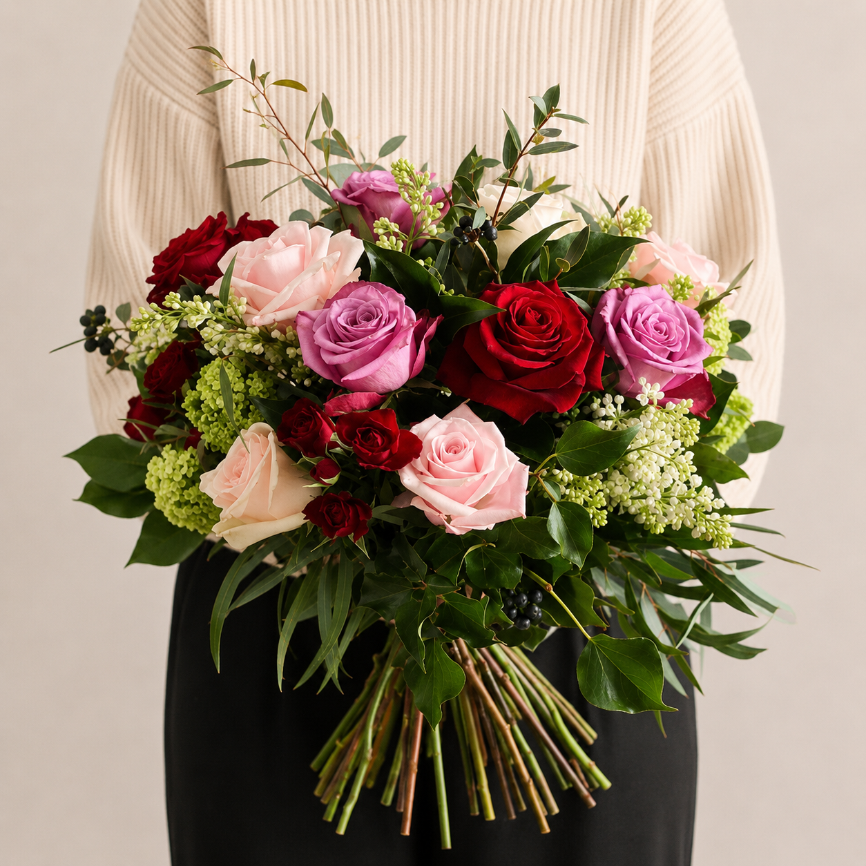 Lady in beige top holding large bouquet of fresh roses, pink red and purple flowers with foliage