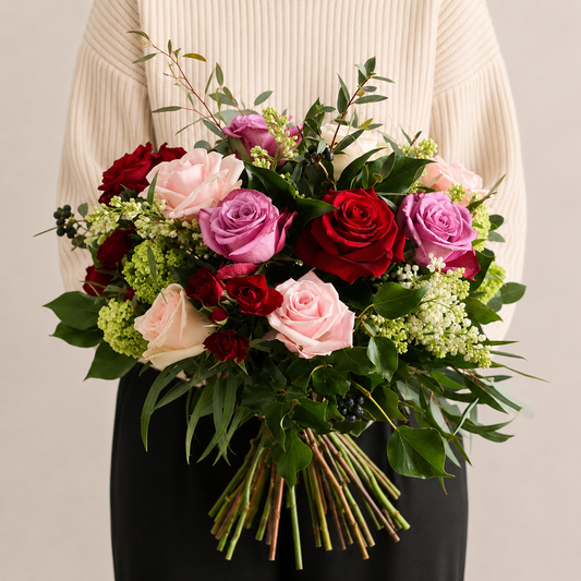 Lady in beige top holding large bouquet of fresh roses, pink red and purple flowers with foliage