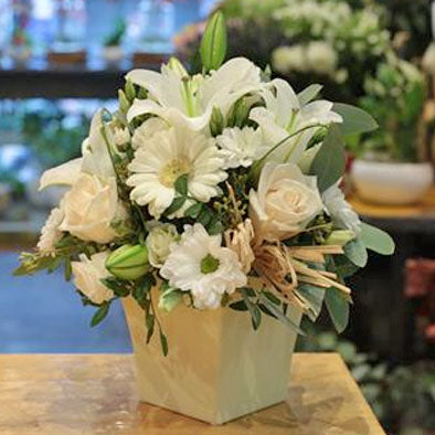 Bouquet of white flowers in a pot on a wooden surface with a blurred background