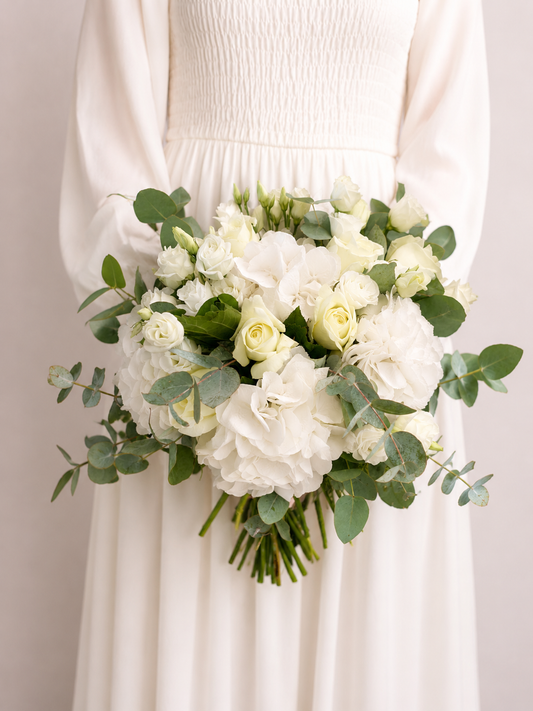 Bride holding Snowdrift Elegance Bridal Bouquet featuring white hydrangeas, ivory roses, spray roses and eucalyptus foliage.