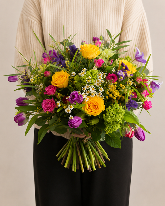 Lady in beige sweater holding a beautiful bouquet of brightly coloured Spring flowers