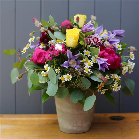 Colorful flower arrangement in a vase on a wooden table with a gray wall background