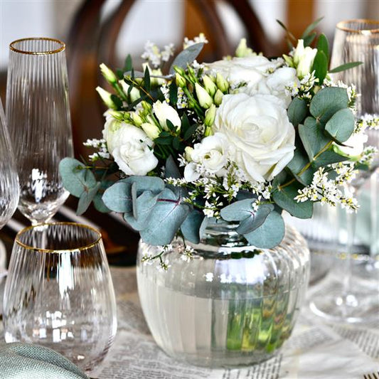 Bouquet of white flowers in a clear vase on a table with glasses.