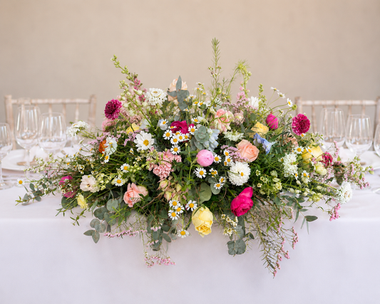 Wildflower Meadow wedding top table arrangement featuring garden roses, daisies, ranunculus, seasonal wildflowers and flowing foliage.