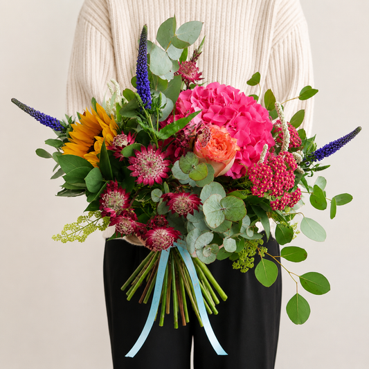 Bouquet of colourful flowers held by a person wearing a white sweater.